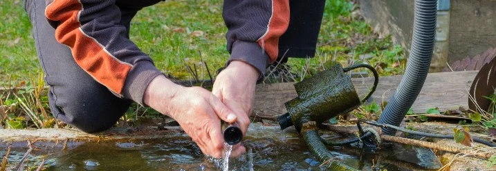 Person reinigt Teichpumpe